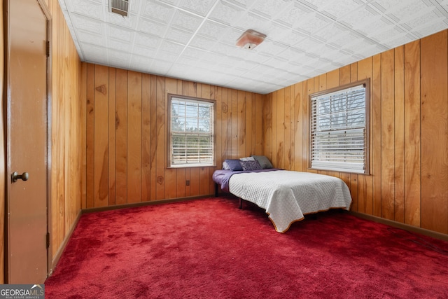 bedroom featuring visible vents, baseboards, wooden walls, and carpet flooring