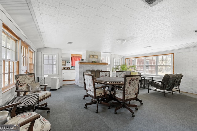 carpeted dining space with plenty of natural light, lofted ceiling, brick wall, and a fireplace