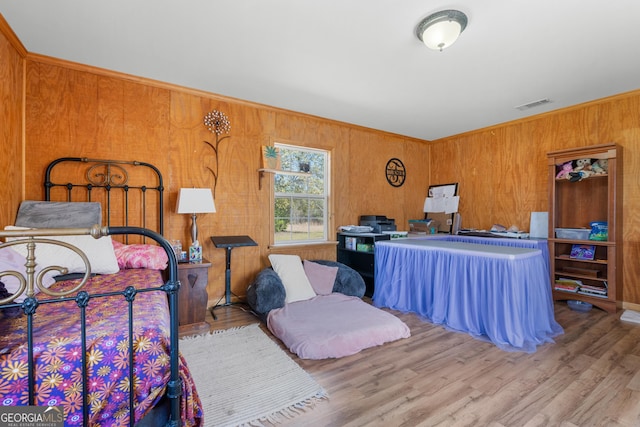 bedroom featuring crown molding, wooden walls, wood finished floors, and visible vents
