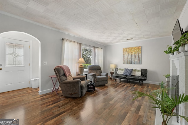 living room with crown molding, baseboards, arched walkways, and wood-type flooring