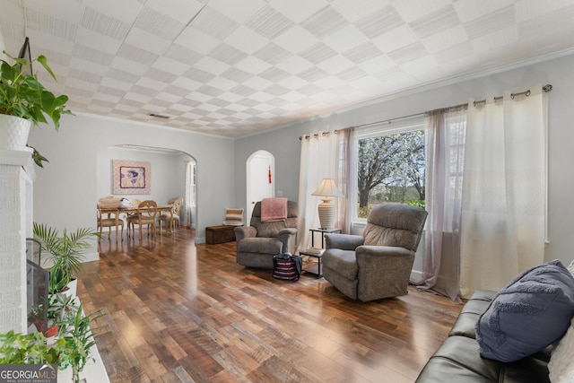 living area featuring visible vents, arched walkways, ornamental molding, and hardwood / wood-style flooring