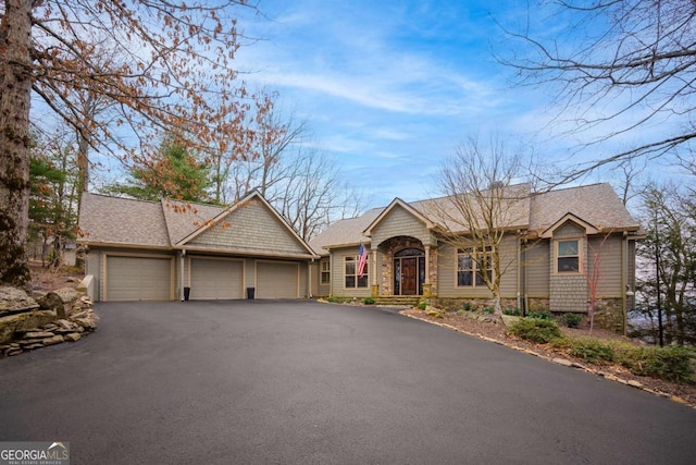 ranch-style house with an attached garage, driveway, a shingled roof, and stone siding