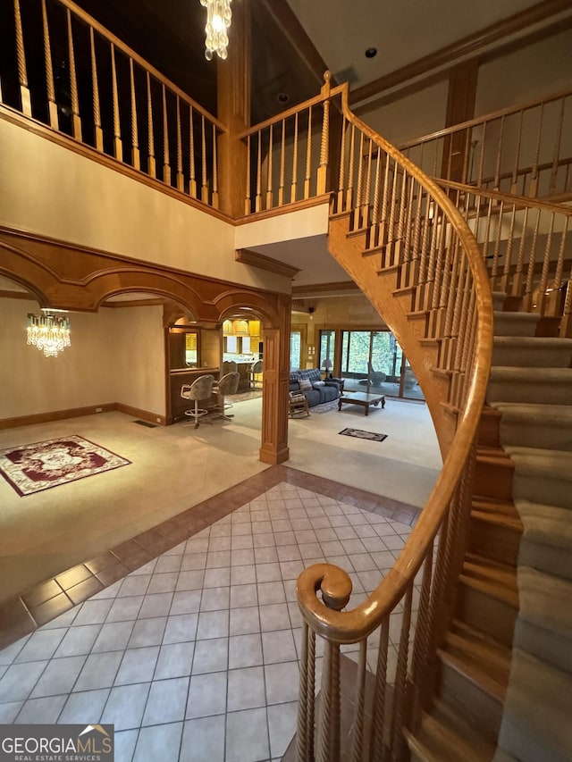 stairway with arched walkways, a high ceiling, a notable chandelier, and tile patterned floors