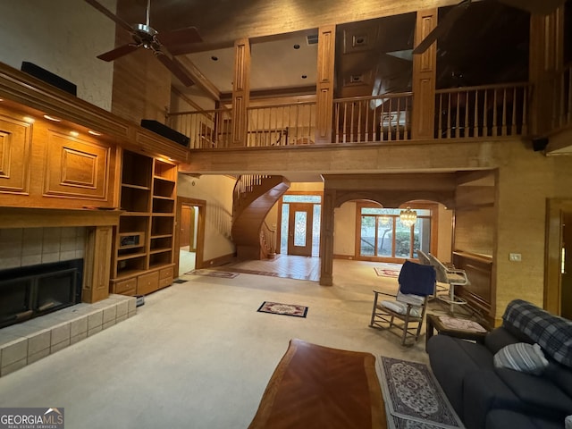 living room with a ceiling fan, a tile fireplace, arched walkways, and a high ceiling