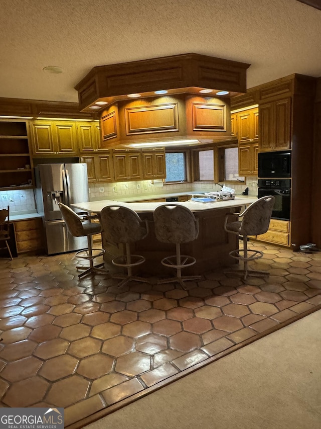 kitchen featuring black appliances, a kitchen bar, light countertops, and brown cabinetry