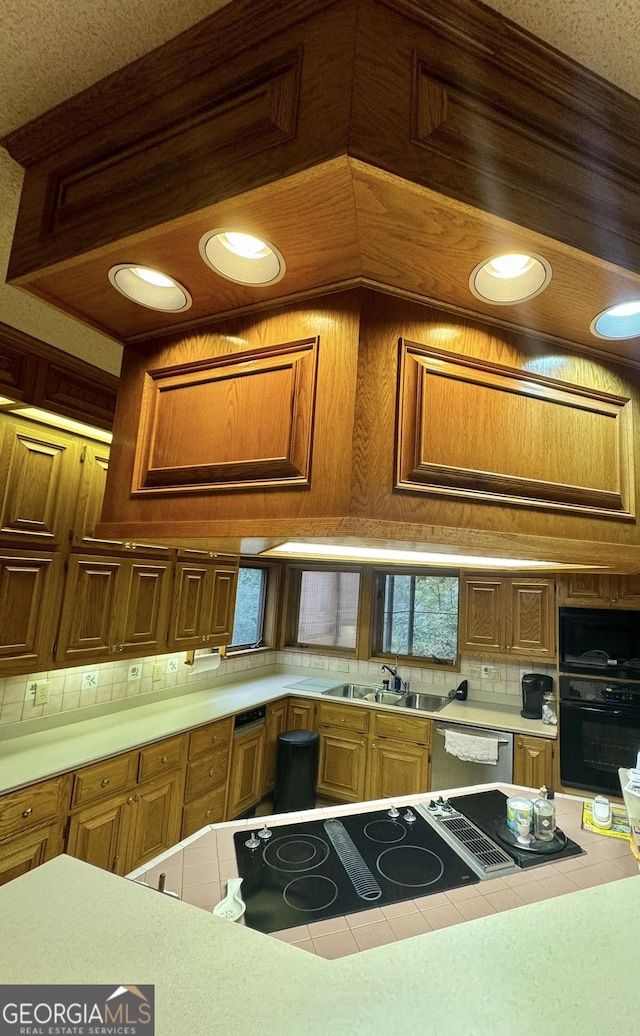 kitchen featuring decorative backsplash, tile countertops, brown cabinets, black appliances, and a sink