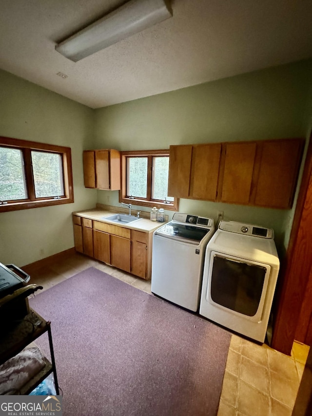 kitchen with baseboards, brown cabinetry, light countertops, washing machine and dryer, and a sink