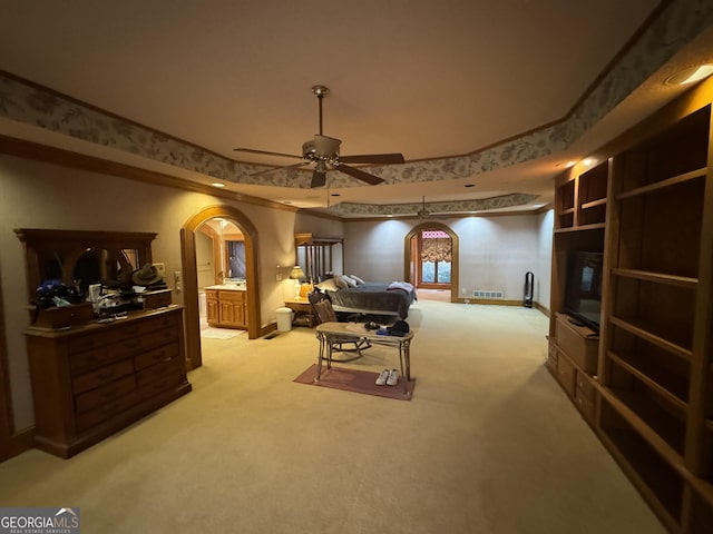 bedroom with baseboards, arched walkways, a raised ceiling, connected bathroom, and light colored carpet