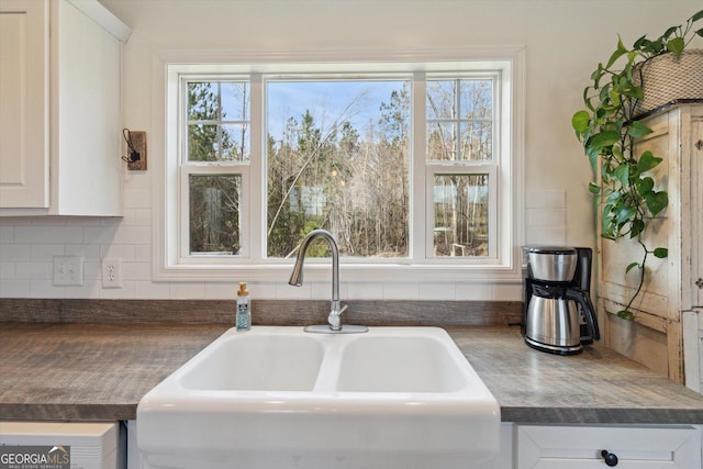 kitchen with decorative backsplash, dark countertops, white cabinets, and a sink