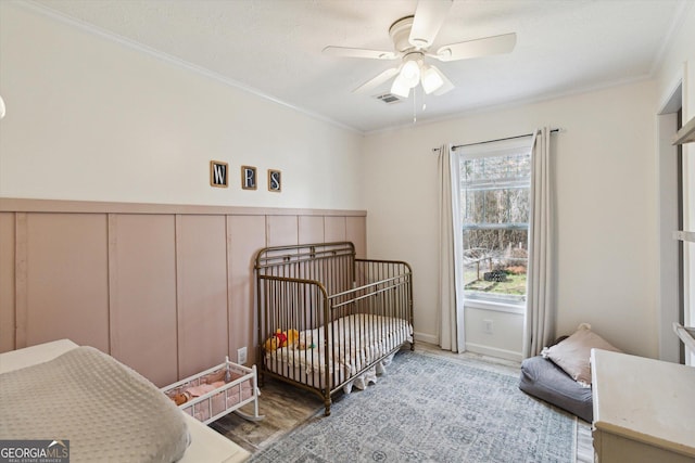 bedroom with a nursery area, a ceiling fan, visible vents, and ornamental molding