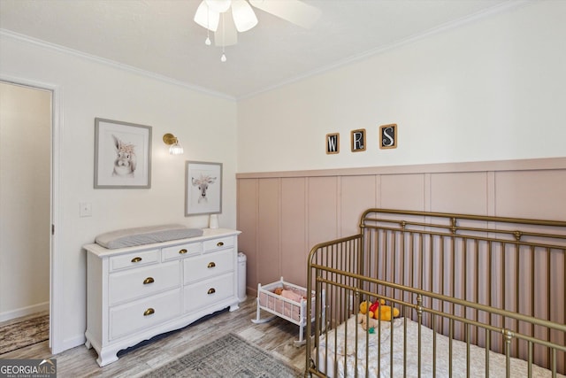 bedroom with a wainscoted wall, a crib, crown molding, and light wood-style floors