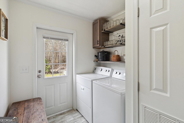 clothes washing area featuring cabinet space, light wood-style flooring, crown molding, and washer and clothes dryer