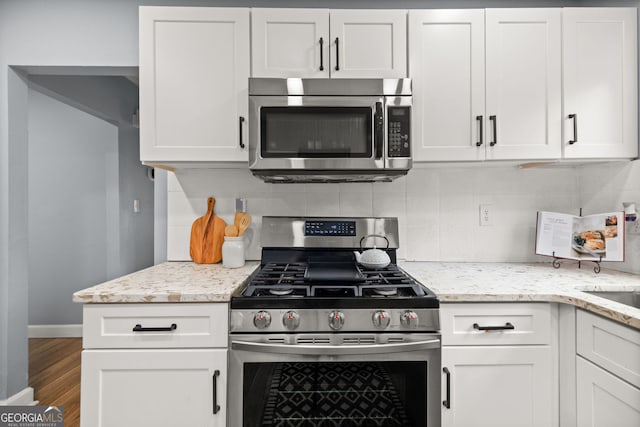 kitchen featuring tasteful backsplash, light stone counters, appliances with stainless steel finishes, wood finished floors, and white cabinetry