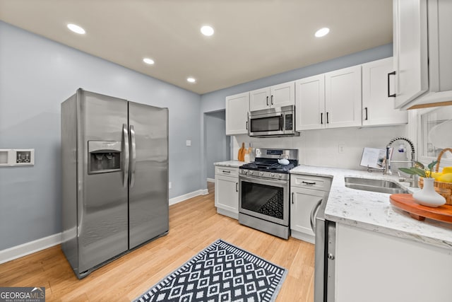 kitchen featuring light wood-style floors, appliances with stainless steel finishes, light stone counters, and a sink