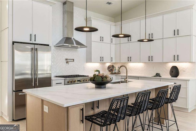 kitchen with tasteful backsplash, high end fridge, light stone countertops, a sink, and exhaust hood