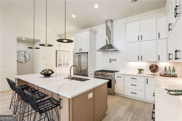 kitchen with light wood-style flooring, a sink, high quality appliances, wall chimney range hood, and decorative backsplash