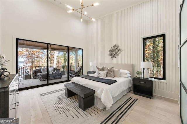 bedroom with access to outside, a high ceiling, light wood-style flooring, and an inviting chandelier