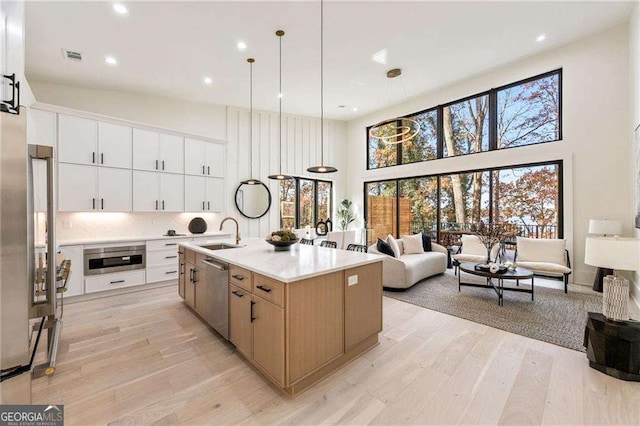 kitchen featuring a towering ceiling, stainless steel dishwasher, light wood-style floors, open floor plan, and a sink