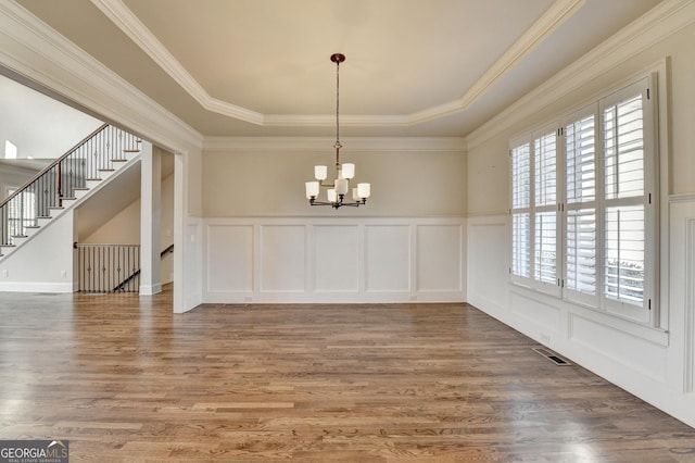 unfurnished dining area featuring a chandelier, a decorative wall, wood finished floors, visible vents, and a tray ceiling