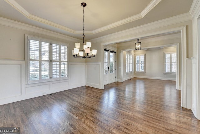 unfurnished dining area featuring visible vents, wood finished floors, crown molding, a decorative wall, and a notable chandelier