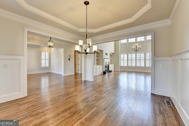 unfurnished dining area with an inviting chandelier, a fireplace, wood finished floors, and wainscoting