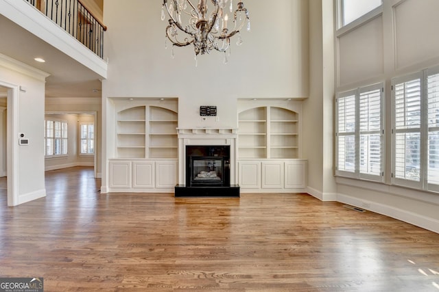 unfurnished living room featuring a glass covered fireplace, baseboards, a high ceiling, and wood finished floors