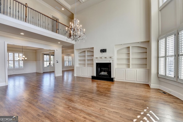 unfurnished living room with built in shelves, a glass covered fireplace, light wood-style flooring, and an inviting chandelier