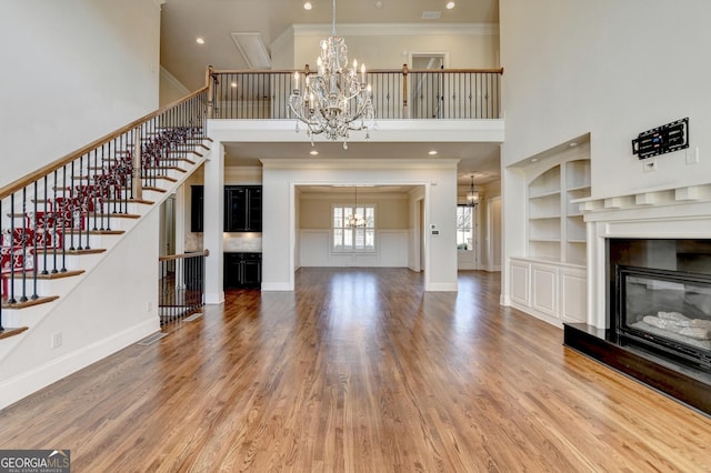 unfurnished living room featuring crown molding, wood finished floors, a glass covered fireplace, and a notable chandelier