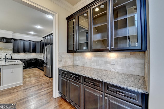 kitchen with light stone counters, a sink, freestanding refrigerator, light wood finished floors, and crown molding