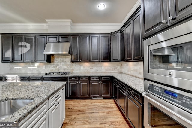 kitchen with appliances with stainless steel finishes, backsplash, light wood-style floors, and under cabinet range hood