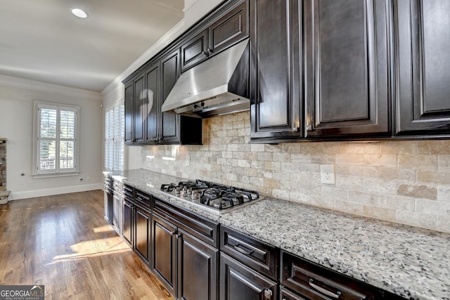 kitchen with wood finished floors, light stone countertops, crown molding, under cabinet range hood, and stainless steel gas cooktop