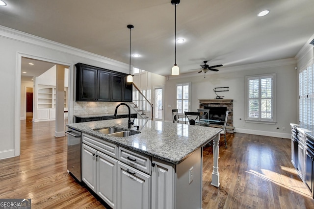 kitchen with crown molding, dark wood finished floors, a sink, and a stone fireplace