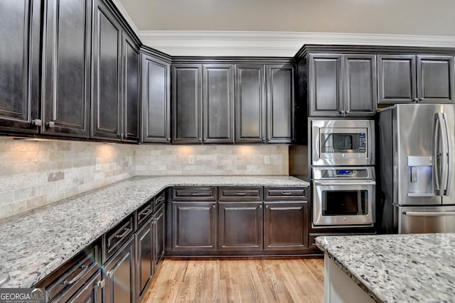 kitchen with appliances with stainless steel finishes, light stone counters, light wood finished floors, and tasteful backsplash