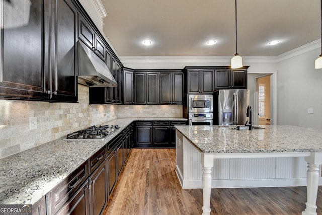 kitchen featuring light stone counters, under cabinet range hood, a sink, appliances with stainless steel finishes, and crown molding