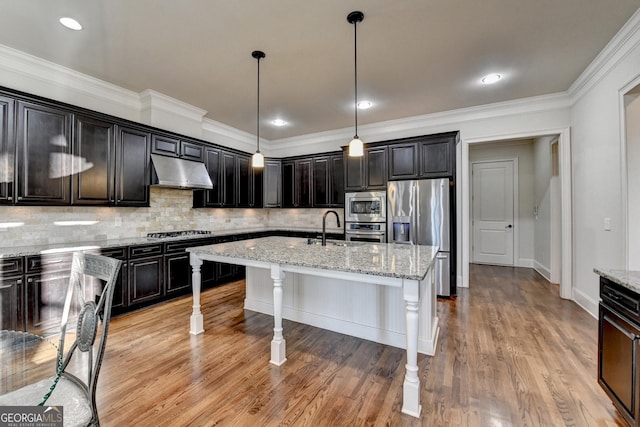 kitchen with under cabinet range hood, a kitchen breakfast bar, appliances with stainless steel finishes, decorative backsplash, and a center island with sink