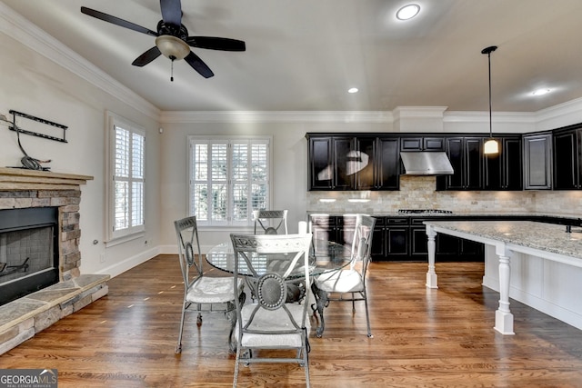 dining space with baseboards, ceiling fan, ornamental molding, light wood-style floors, and a fireplace