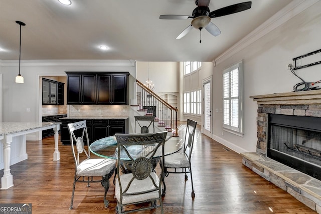 dining room featuring a stone fireplace, dark wood-style flooring, baseboards, stairs, and crown molding