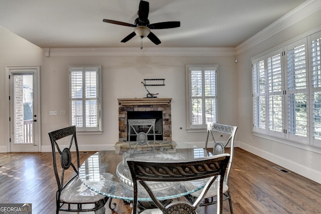 dining space with a healthy amount of sunlight, a fireplace, ornamental molding, and wood finished floors