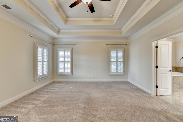 carpeted empty room with ornamental molding, a raised ceiling, visible vents, and baseboards