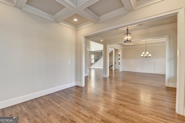 unfurnished room featuring a notable chandelier, coffered ceiling, beam ceiling, light wood finished floors, and crown molding