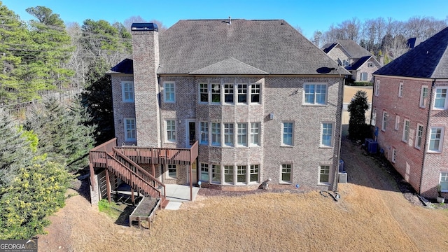 back of property featuring a wooden deck, stairs, a chimney, and brick siding