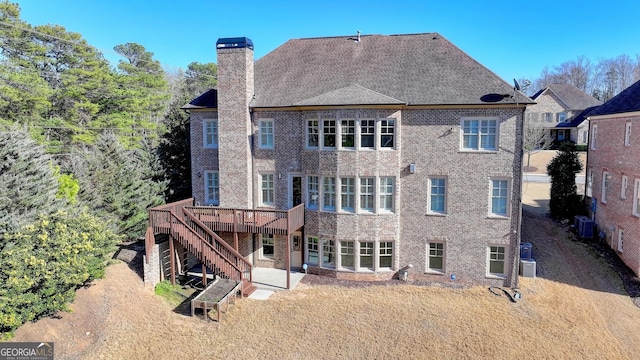 rear view of house featuring a chimney, stairway, a wooden deck, central air condition unit, and brick siding