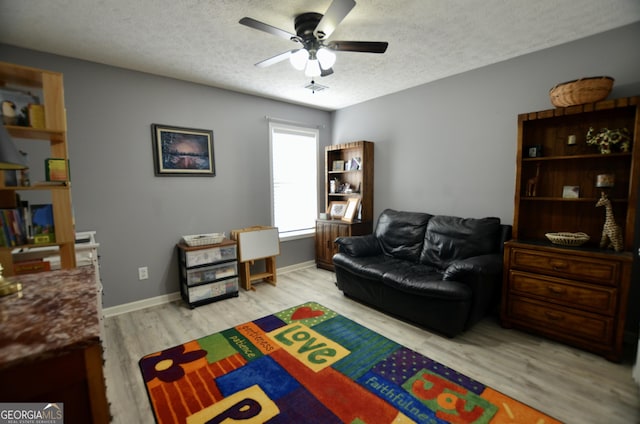 rec room with a textured ceiling, ceiling fan, light wood finished floors, and baseboards