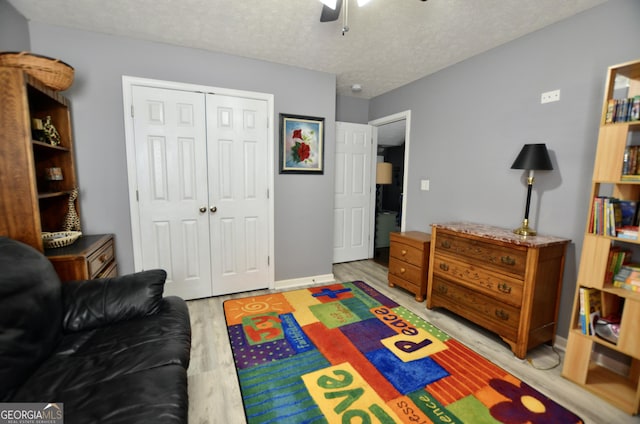 bedroom with a textured ceiling, ceiling fan, baseboards, light wood-style floors, and a closet