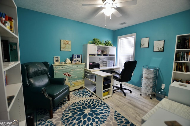 office space with a textured ceiling, ceiling fan, wood finished floors, and visible vents