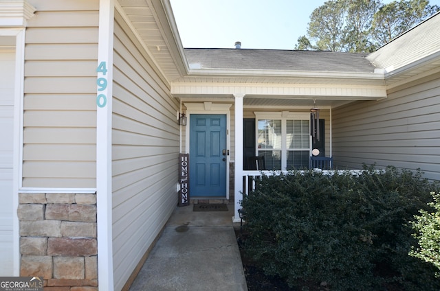 property entrance with covered porch, stone siding, and roof with shingles