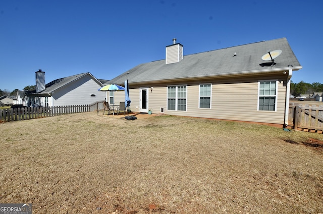 rear view of house featuring a fenced backyard, a yard, and a chimney