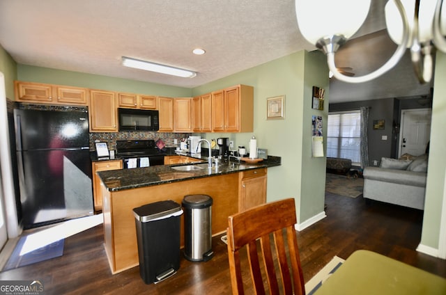 kitchen with dark wood finished floors, dark stone counters, a peninsula, black appliances, and a sink