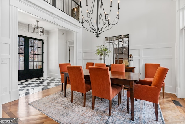 dining area featuring french doors, a decorative wall, a notable chandelier, and light wood finished floors