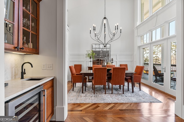 dining room featuring a decorative wall, a towering ceiling, beverage cooler, indoor wet bar, and an inviting chandelier